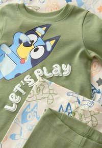 Groen katoen pyjama set met een cartoonhond graphic en de tekst "Laten we spelen", in combinatie met crème- en blauwe broek met een patroon van de hond.
