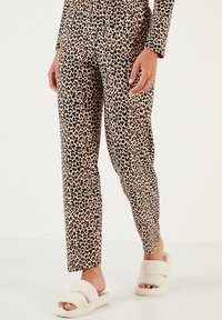 Pantalone s uzorkom leoparda od mekanog materijala, s bež podlogom i smešnim i crnim mrljama. Upareni s belim pahuljastim papučama.