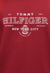 Κόκκινο βαμβακερό μπλουζάκι με λευκό κείμενο που γράφει «TOMMY HILFIGER», με τις λέξεις «NEW YORK CITY» και ένα λογότυπο από κάτω.