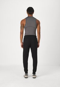 Grå ærmeløs top med et tætsiddende design, parret med sorte joggerbukser med elastiske manchetter. Enkel, glat tekstur hele vejen igennem.