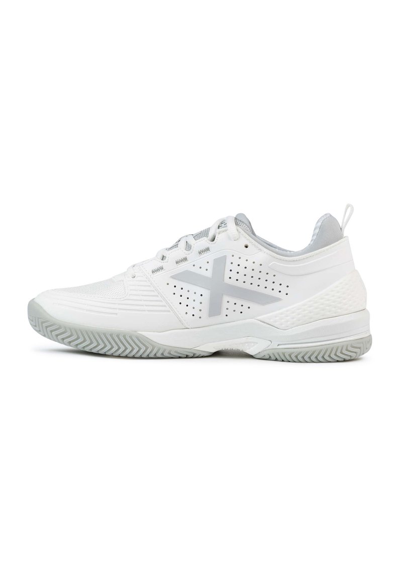 Zapato deportivo blanco con parte superior de malla, detalles perforados y un logo gris. Presenta una suela texturizada y un diseño de talón que brinda soporte.