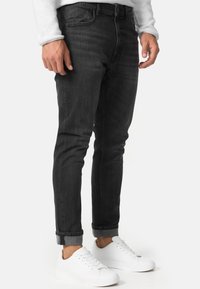Jeans skinny negros de mezclilla, con un diseño de cinco bolsillos y bajos remangados, combinados con zapatillas blancas para crear contraste.