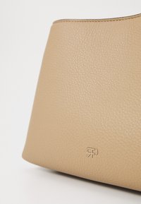 Borsa a mano in pelle color cuoio con superficie testurizzata e logo in rilievo. Il design presenta una forma arrotondata e accenti minimalisti.