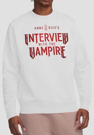 Person trägt ein weißes Sweatshirt mit rotem Text auf der Vorderseite, der "Anne Rices Interview mit dem Vampir" lautet.