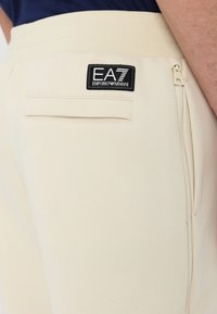 Joggers beige en tissu doux, dotés d'une poche zippée et d'un patch logo noir EA7 Emporio Armani au dos.