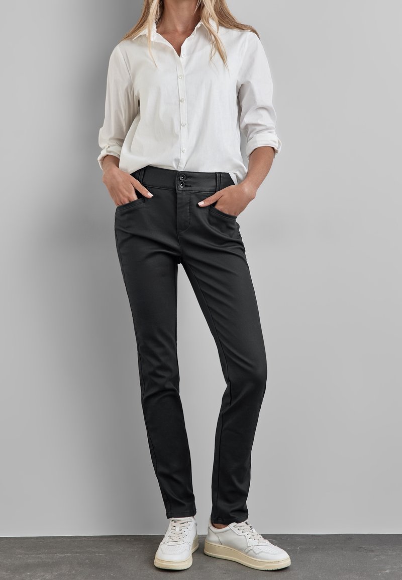 Valkoinen pitkähihainen nappipaita, yhdistetty mustiin kapeisiin housuihin ja valkoisiin lenkkareihin. Paidassa on etutaskut ja sileä kangas.