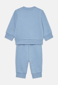 Conjunto de sweatshirt azul claro e calças combinando. Os itens apresentam punhos canelados e uma textura suave, projetados para conforto e facilidade de movimento.