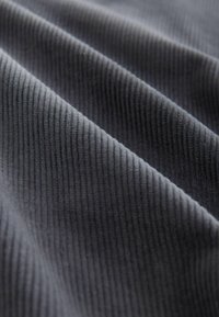 Gray ribbed fabric with pronounced texture, showcasing soft fibers and a wavy drape. The surface features a subtle sheen under light.