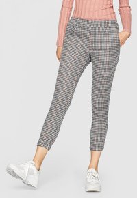 Pantalons à carreaux en noir, blanc et rose avec un design court et une taille élastique. Associés à des baskets blanches.