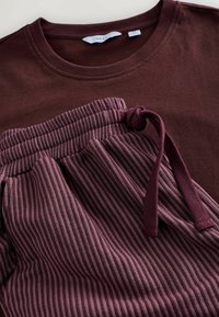 Burgunderrotes T-Shirt und gestreifte bordeauxrote Jogginghose mit elastischem Bund und Kordelzug. Weiche Textur, lässiges Design und harmonisches Farbschema.