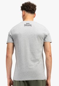Siva pamučna majica s kratkim rukavima, s malim printanim logom na gornjem dijelu leđa u crnoj boji, okrugli izrez i glatka tekstura.