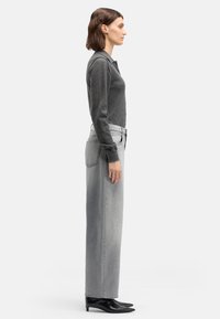 Szary pulower i szare jeansy z wysokim stanem, widok z boku. Gładka tekstura, luźny krój oraz czarne, spiczaste botki dopełniają strój.