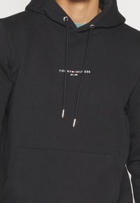 Czarna bluza z kapturem i sznurkami, z logo w białym i czerwonym tekście. Wykonana z gładkiego materiału z przednią kieszenią typu kangur.