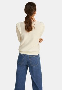 Kremowy sweter dzianinowy z bufkami i prążkowanym dołem, w połączeniu z jasnoniebieskimi spodniami typu wide-leg z wysokim stanem i kieszeniami z tyłu.