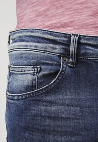 Jeans i denim med en mörkblå tvätt, som har en framficka, en metalldekorationsknapp och stickade detaljer längs midjan.