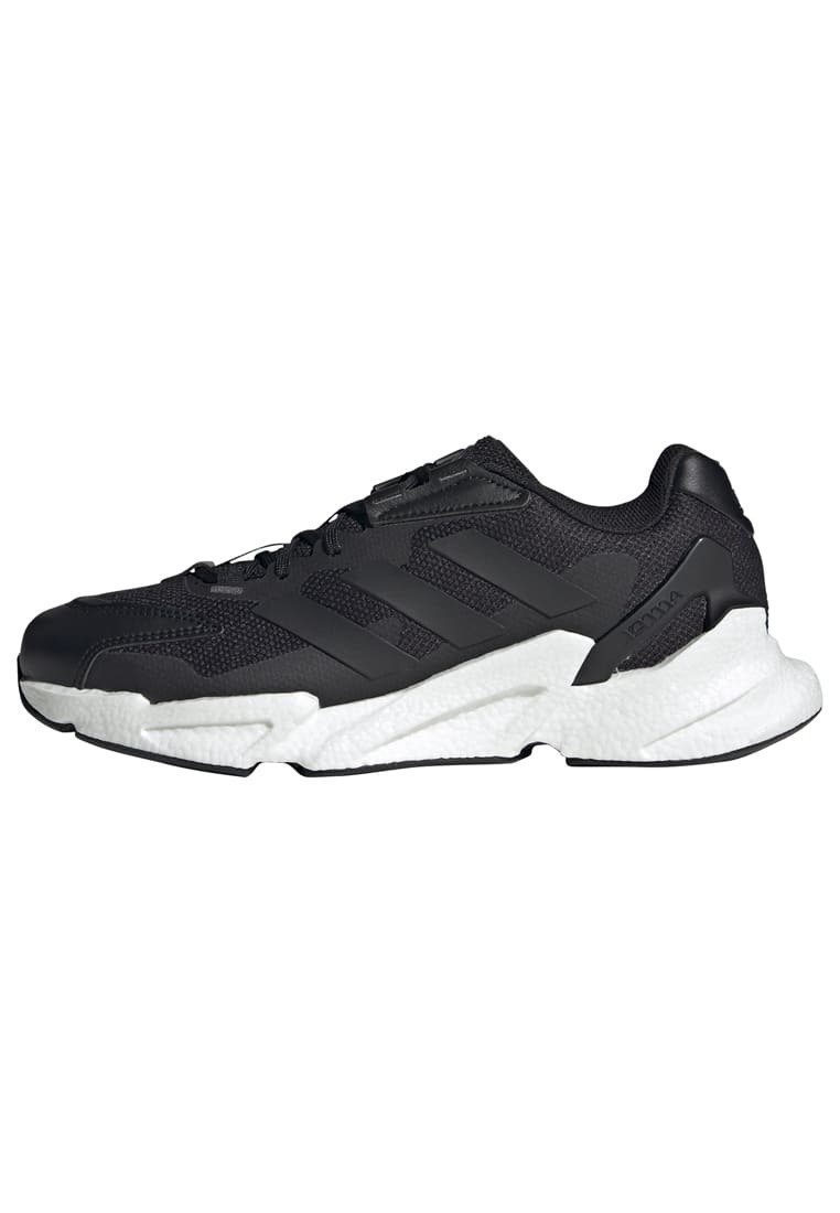 Zapatilla deportiva negra con parte superior de malla, tres rayas negras en el lateral y suela blanca texturizada. Presenta un cuello acolchado y sistema de cordones.