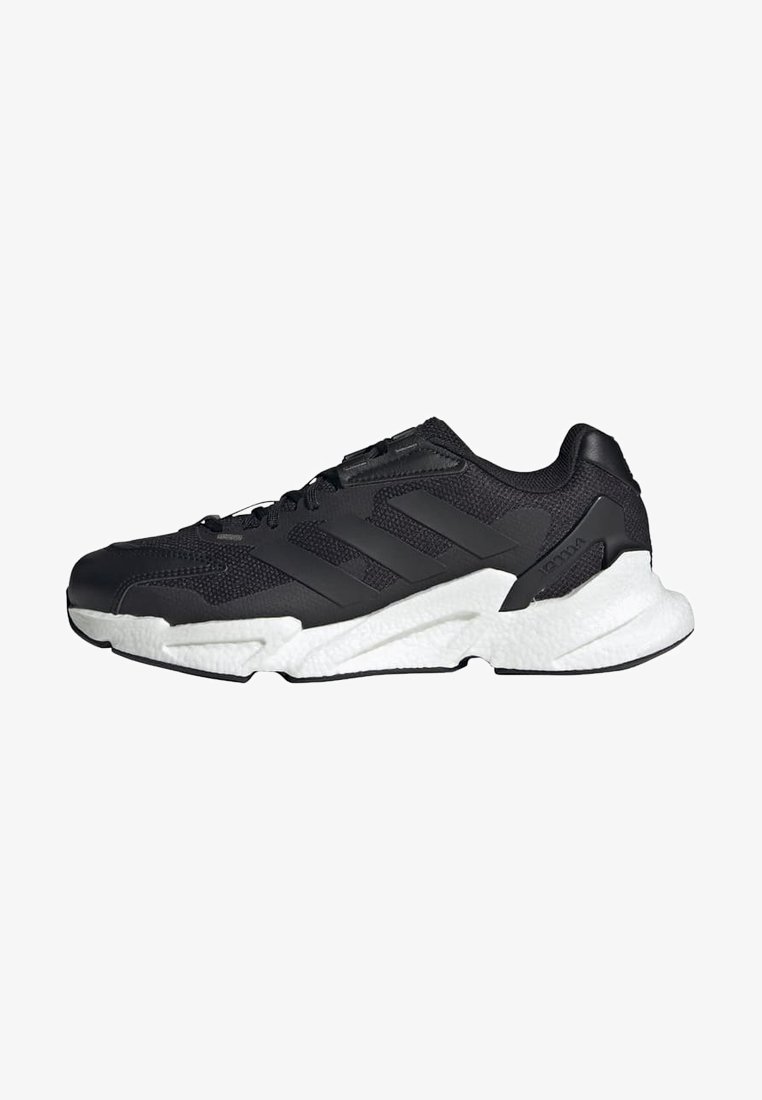 Scarpa sportiva nera con upper in mesh, tre righe nere sul lato e suola bianca texture. Presenta un collare imbottito e un sistema di allacciatura.