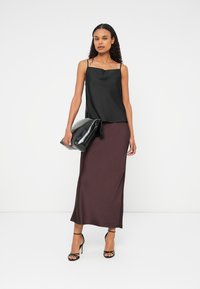 Fekete szatén camisole topp vékony pántokkal, burgundi szatén maxi szoknyával párosítva. A modell egy nagy fekete táskát tart, és pántos magassarkút visel.