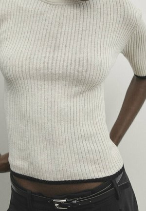 Prążkowany krótki top dzianinowy w jasnobeżowym kolorze z ciemną lamówką, o dopasowanym kroju i krótkich rękawach. Miękka tekstura i subtelny połysk.