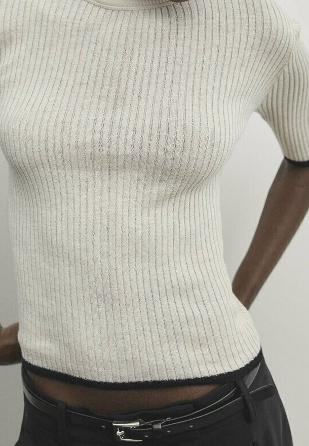 Haut court en maille côtelée beige clair avec bordure foncée, doté d'une coupe ajustée et de manches courtes. Texture douce et léger éclat subtil.