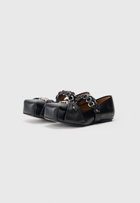 Pantofi din piele neagră cu vârf rotund, accent decorativ cu lanț și detalii pliate pe partea superioară. Talpă plată cu un design minimalist.