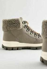 Khaki buty trekkingowe z teksturowanym wełnianym kołnierzem, metalowymi oczkami i beżowymi sznurowadłami; z wytrzymałą podeszwą zapewniającą przyczepność.