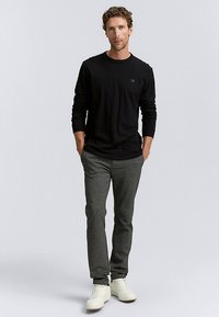 Black long-sleeve shirt with round neckline, paired with gray patterned trousers and white sneakers, displayed on a neutral background.