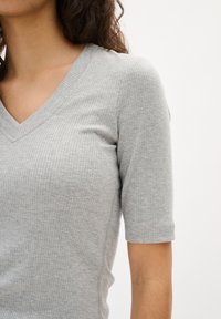 Ljusgrå ribbad stickad topp med V-ringning och korta ärmar. Texturen är mjuk och lätt t�öjbar, sitter tajt mot kroppen.