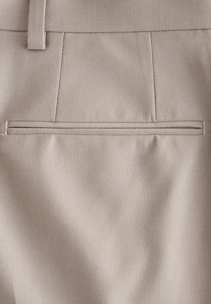 Tissu beige à texture lisse, doté d'une poche passepoilée rectangulaire au-dessus d'une ligne de couture, design simple et ajusté.