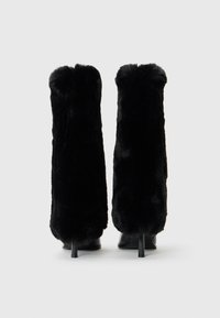 Botas de tacón alto de piel sintética negra que presentan un diseño elegante, caña alta y puntas redondeadas, con tacones delgados y afilados que aportan mayor altura.