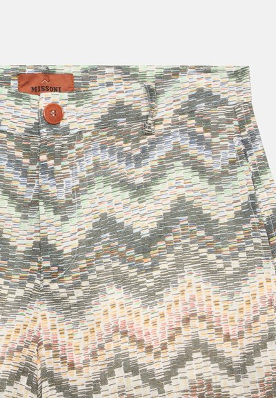 Gros plan sur un pantalon à motifs zigzag multicolores avec une taille boutonnée et une étiquette Missoni marron sur un tissu clair.