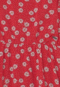 Rode stoffen jurk met een bloemenpatroon van witte madeliefjes met gele centra en kleine witte stippen. Geverpunte taille detail.