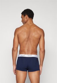 Caleçons navy avec une ceinture blanche arborant le logo Lacoste, vus de l'arrière, mettant en valeur la texture du tissu et la coupe.
