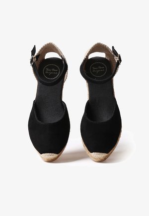 Sandalias espadrilles negras con correas en el tobillo, suelas envueltas en yute y punteras cerradas, vistas desde arriba sobre fondo blanco.