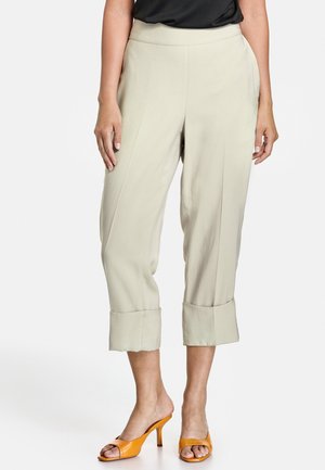 Pantalon beige court avec ourlets retroussés porté avec un haut noir et des sandales à talons ouvertes orange.