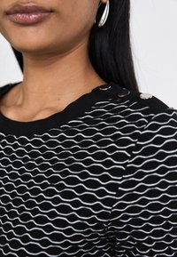 Black knit top featuring a wavy white pattern, textured surface, and silver button accents on the shoulder.