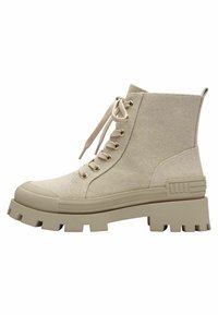 Bottine beige avec une tige en tissu texturé, bout rond, semelle plate, et œillets dorés. Présente un design à lacets sur le devant.