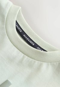 Světle zelené bavlněné tričko s žebrovaným kulatým výstřihem; u límce je černá etiketa s nápisem "ALLSAINTS". Hladká textura.