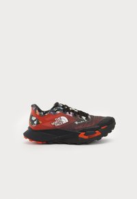 Herresneakers med sort gummi såle, rød og mønstret mesh-overdel, har en hvit logo og sorte snørebånd. Mønsteret på sålen er fremtredende.