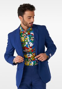 Royalblauer Anzugjackett, das über einem bunten Grafikhemd mit Cartoon-Charakteren getragen wird; das Outfit enthält gemusterte Akzente und eine Uhr.