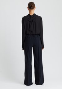 Zwarte blouse met een gestrikte strik bij de kraag, gecombineerd met hoog - taille, wijde donkere broeken. Gladde stof met een gestructureerde vorm.