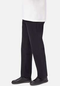 Person wearing straight black pants paired with black leather lace-up shoes and a white shirt against a plain background.