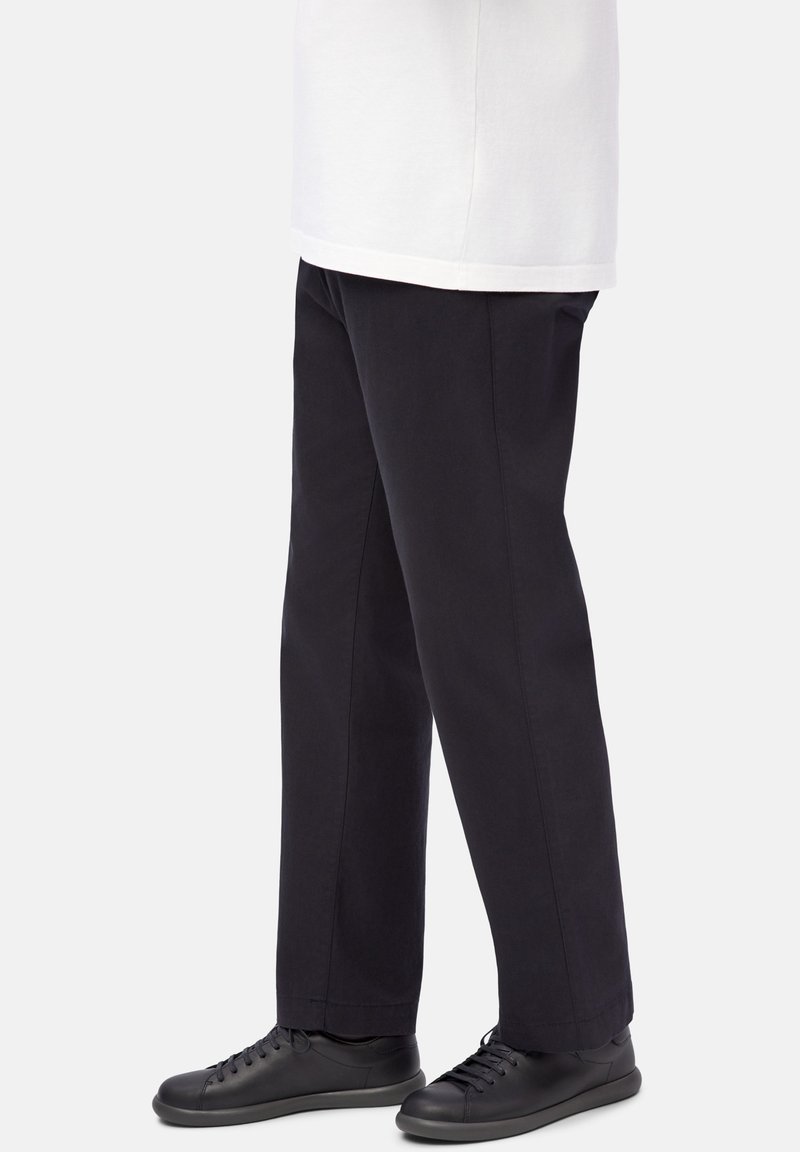 Person wearing straight black pants paired with black leather lace-up shoes and a white shirt against a plain background.