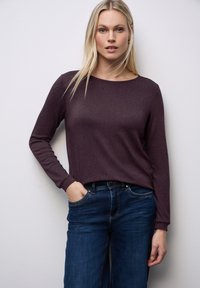 Długirękawowa bluzka w ciemnopurpurowym kolorze, wykonana z gładkiego, błyszczącego materiału, połączona ze średnio-pranym, lekko luźnym niebieskimi dżinsami.