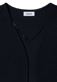 Haut noir texturé à manches longues avec un col en V et une étiquette blanche à l'intérieur du col indiquant "CECIL".