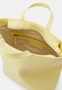 Sac à main en cuir jaune avec deux poignées, fermeture éclair sur le dessus ouverte et poche intérieure zippée avec doublure en tissu beige.