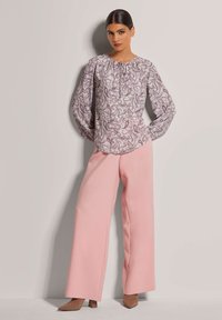 Helles lila Paisley-Bluse mit langen Ärmeln und gerafftem Ausschnitt; kombiniert mit hochtaillierten pinken weitgeschnittenen Hosen und beigen spitzen Absätzen.