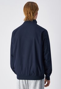 Navy blue windbreaker jacket with a high collar, elastic cuffs, and waistband. Smooth texture, lightweight fabric, minimal design.