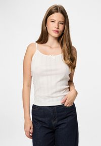 Camisola bianca a maglia con spalline sottili, caratterizzata da un piccolo fiocco sul collo e un motivo a righe testurizzato. Abbinata a jeans blu scuro.