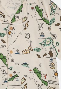 Kortermet skjorte i lys beige stoff med et fargerikt karttrykk som viser landområder, båter, skyer og solmotiver; treknapper.